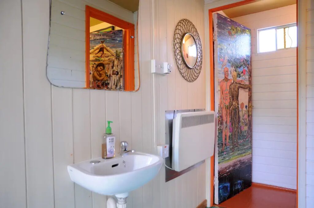 A shared bathroom with a sink and a decoupage door of two human figures and a tree.